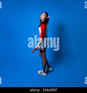 Jeune femme en Harlequin Costume debout devant un fond bleu avec espace de copie Banque D'Images