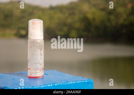 Bouteille d'encre d'imprimante vide sur béton bleu avec fond de lac et de montagnes tropicales, dans un style de prise de vue créatif, avec espace négatif pour le texte. Banque D'Images