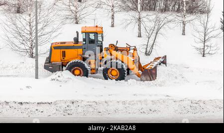 Déneigement. Le tracteur se dégage après de fortes chutes de neige. Un gros tracteur orange élimine la neige de la route et dégage le trottoir. Nettoyage des routes Banque D'Images