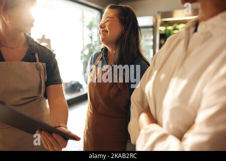 Une femme heureuse avec le syndrome de Down souriant gaiement tout en se tenant dans une réunion du personnel dans une épicerie. Groupe de diverses femmes travaillant ensemble dans un Banque D'Images