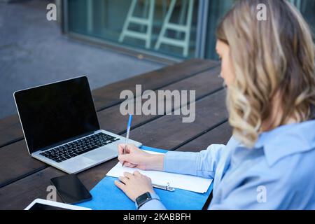 Gros plan portrait d'une femme étudiante assister à des cours en ligne, assis à l'extérieur à l'air frais avec un ordinateur portable et prendre des notes. Chat vidéo femme d'affaires Banque D'Images