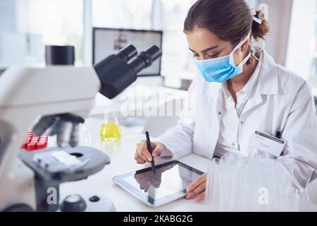 Cette tablette a facilité le travail en laboratoire. Une jeune scientifique ciblée portant un masque chirurgical et travaillant sur une tablette numérique Banque D'Images