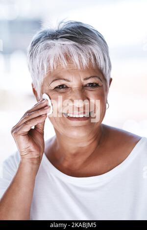 Elle s'en va toujours pour le look naturel. Portrait d'une femme mûre et gaie appliquant un démaquillant sur son visage tout en regardant l'appareil photo. Banque D'Images