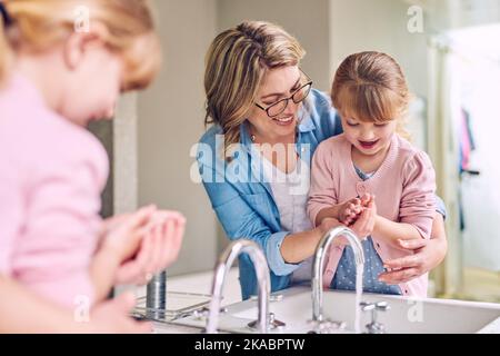 Je le fais bien maman, une jeune mère gaie et sa petite fille se lavant les mains ensemble. Banque D'Images