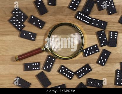 Pièces de jeu de Domino éparpillées sur un bureau en bois avec loupe dorée, vue du dessus. Banque D'Images