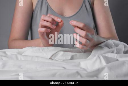 Les mains insérant le fil dans le trou de l'aiguille pour la couture. Concept de concentration et d'attention. Banque D'Images
