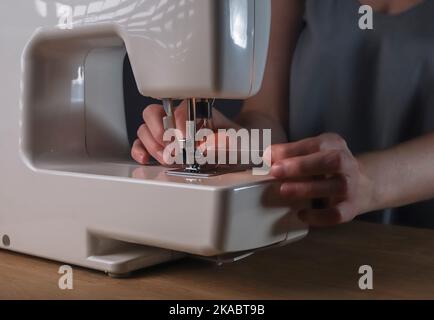 Les mains insérant le fil dans le trou de l'aiguille dans la machine à coudre, détails. Banque D'Images