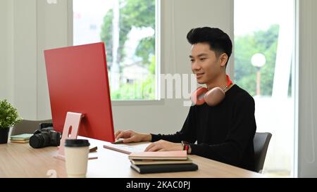 Souriant, des éditeurs de photos asiatiques retouchant des photos sur un ordinateur personnel, travaillant dans un bureau créatif Banque D'Images