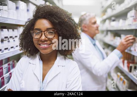 Venez nous rendre visite pour toute douleur ou gêne. Portrait d'une jeune pharmacienne gaie debout avec les bras repliés tout en regardant l'appareil photo dans un Banque D'Images