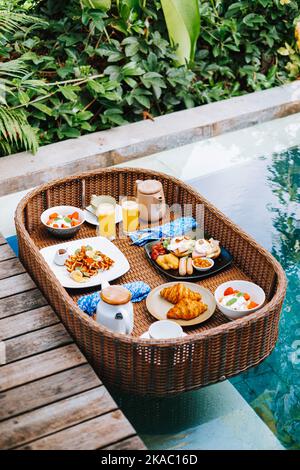 Le plateau de petit-déjeuner en rotin synthétique ou en bambou flotte au coin de la piscine Banque D'Images