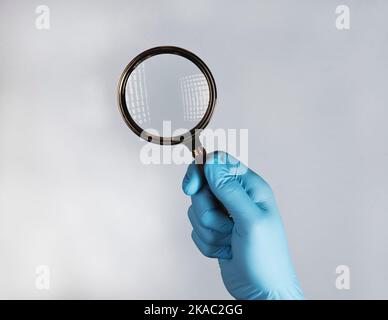 Main dans un gant médical avec loupe, recherche et examen de maladies avec la vitre. Banque D'Images