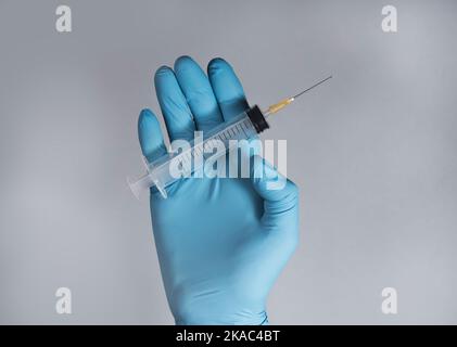 Nettoyer la seringue avec une aiguille pointue dans les mains des médecins dans le gant sur fond bleu gris. Banque D'Images