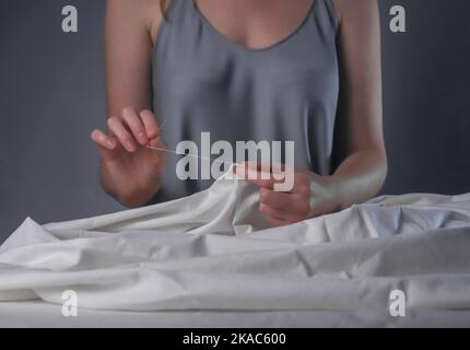 Les mains insérant le fil dans le trou de l'aiguille pour coudre à son bureau en bois. Banque D'Images