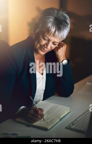 Le succès prend du temps et de la planification. Une femme d'affaires mûre écrivant dans un bloc-notes pendant une nuit de travail. Banque D'Images