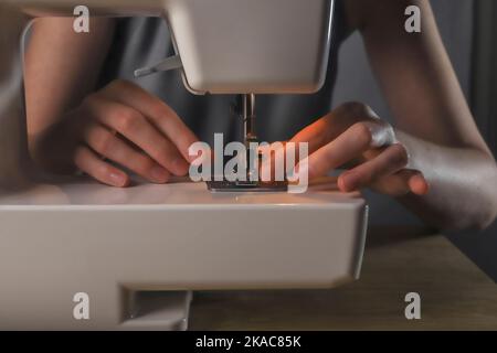 Les mains insérant le fil dans le trou de l'aiguille dans la machine à coudre, détails. Banque D'Images