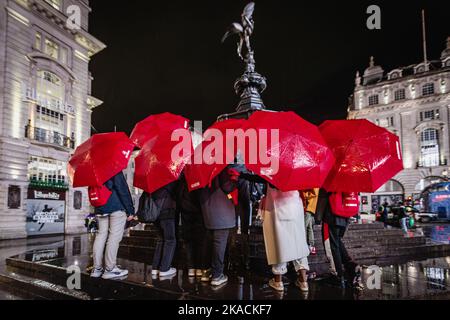 Congrégation des parasols rouges du touriste kazakh à l'abri de la pluie sous Anteros à Piccadilly Circus à Londres. Banque D'Images