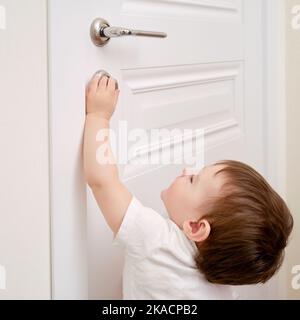 Bébé ouvre la serrure, la main de l'enfant se ferme. Porte en bois blanc, poignée de porte en métal et main de bébé Banque D'Images