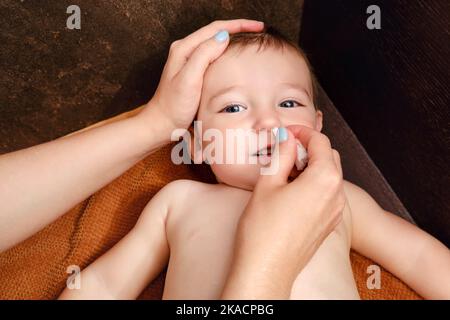 Une mère nettoie son nez avec un tampon en coton torsadé pour un bébé garçon heureux. Maman nettoie les narines d'un enfant souriant. Enfant d'un an Banque D'Images