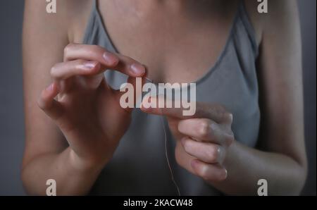 Les mains insérant le fil dans le trou de l'aiguille pour la couture. Concept de concentration et d'attention. Banque D'Images