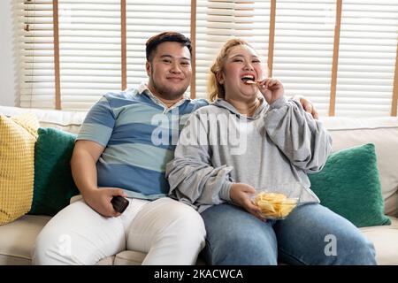 Un jeune couple asiatique de chubby regarde une série télévisée et un film sur le canapé dans le salon. Homme et femme qui s'amusent ensemble à la maison. Les gens rient et sourient ensemble Banque D'Images