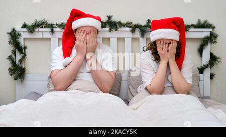 Un homme et une femme pleurent sur un lit décoré pour Noël et le nouvel an, couple familial dans la chambre à coucher Banque D'Images