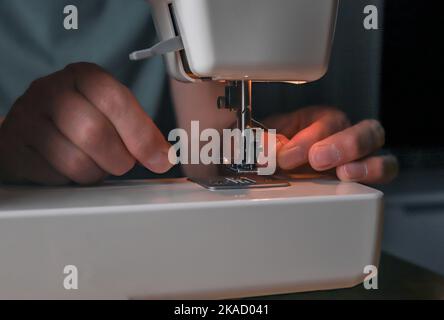 Les mains de sexe masculin insèrent le fil dans le trou de l'aiguille de la machine à coudre, en gros plan. Banque D'Images