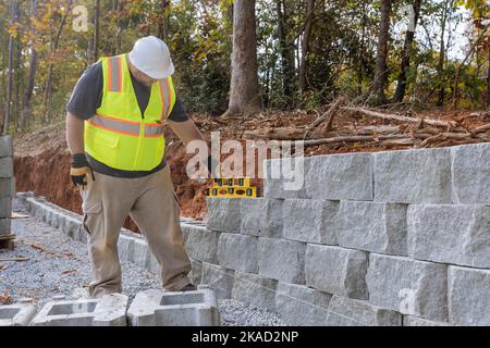 Sur la nouvelle propriété où le mur de bloc de retenue est construit, le travailleur de la construction est en train d'ériger le mur de bloc Banque D'Images