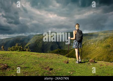 une jeune femme qui fait de la randonnée dans les montagnes, bénéficie d'une vue magnifique sur un paysage verdoyant et d'un ciel spectaculaire Banque D'Images