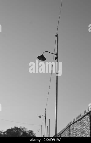 Photo en niveaux de gris d'une rangée de réverbères avec une clôture barbelée en arrière-plan Banque D'Images