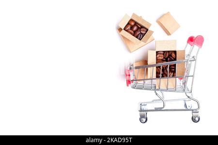 Chariot de supermarché miniature et boîtes en carton contenant des grains de café torréfiés foncés isolés sur fond blanc avec espace de copie. Banque D'Images