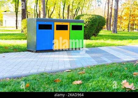 Poubelles colorées pour la collecte et le tri des déchets dans un parc public par temps ensoleillé. Concept d'élimination des déchets. Banque D'Images