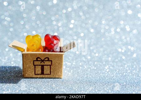 Mélange de bonbons colorés en forme d'ours en gélatine dans une boîte cadeau en carton isolée sur un fond étincelant. Banque D'Images
