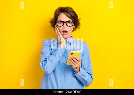 Gros plan photo de jeunes impressionnés jeune étudiant université information tenir téléphone date limite toucher joues confus isolé sur fond jaune couleur Banque D'Images