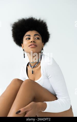 maussée et jeune femme afro-américaine en chemise à manches longues isolée sur blanc, image de stock Banque D'Images