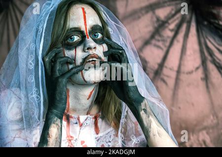 Portrait en gros plan de femme zombie en robe de mariage avec voile et maquillage de scène regardant dans l'appareil photo. Fille a appliqué du maquillage blanc et des taches de sang sur elle Banque D'Images