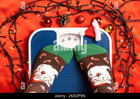 Une femme en chaussettes de Noël se tient sur la balance, se pèse après la gourmandise pendant les vacances Banque D'Images