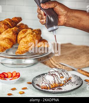 Une personne ajoutant du sirop de chocolat sur un croissant fraîchement cuit Banque D'Images