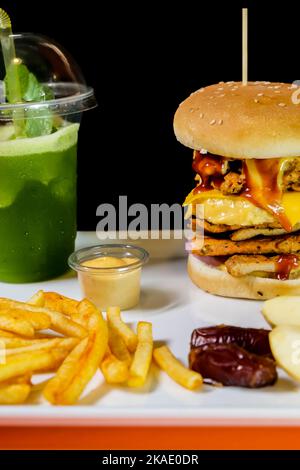 Un gros plan d'un hamburger, de frites et d'une sauce avec des morceaux de pommes et des dattes avec une tasse de jus de menthe sur un plateau blanc Banque D'Images