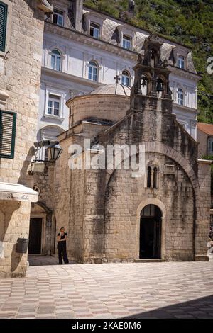 Kotor, Monténégro - 29 avril 2022 : façade d'une église orthodoxe médiévale de Saint Luc dans la vieille ville de Kotor. Une femme vêtue de noir debout sur le mur. Banque D'Images