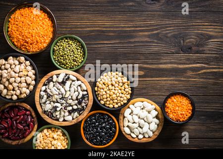 Assortiment de légumineuses, lentilles, pois chikés et haricots dans différents bols sur table en bois.Vue de dessus.Nourriture végétalienne, viande alternative. Banque D'Images