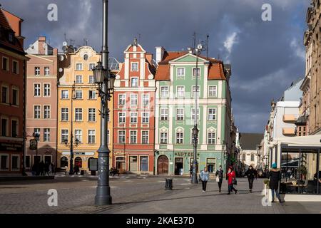 Wroclaw, Pologne - 19 février 2022 : bâtiments résidentiels historiques étroits sur la place de la vieille ville. Les gens qui descendent dans la rue, le ciel orageux. Banque D'Images