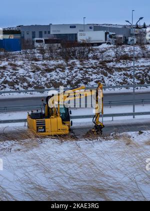 Reykjavik, Islande - 25 janvier 2022: Un véhicule jaune Komatsu PW148 sur roues de pelle hydraulique roulant en bas de la route. Hiver enneigé. Banque D'Images