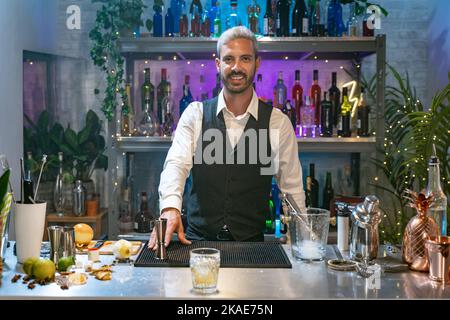 Portrait de Barman dans une chemise blanche et tablier noir souriant regardant l'appareil photo à la fête dans la boîte de nuit. La vie nocturne. Banque D'Images