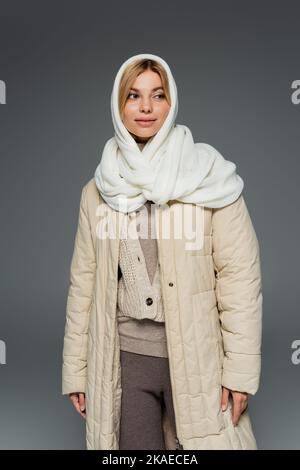 jeune femme élégante en foulard d'hiver et manteau debout isolé sur gris, image de stock Banque D'Images