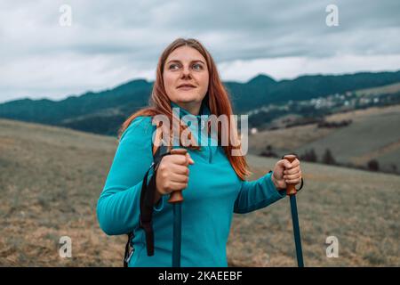 Belle femme heureuse randonneur sentier de randonnée, marche sur colline herbeuse, porte sac à dos, utilisation de bâtons de randonnée, profiter de l'été nuageux journée. Banque D'Images