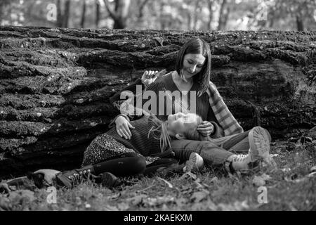 Photo en noir et blanc d'une jeune fille d'âge scolaire couchée sur les jambes d'une mère aimante dans des embrases chaudes, figée tronc d'arbre. Femme et fille sont à l'entrée Banque D'Images