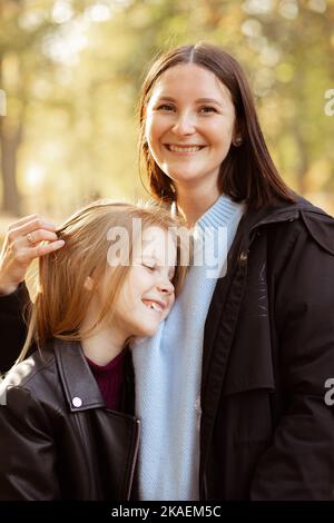 Portrait gros plan de la femme joyeuse appuyant à la poitrine souriant petite fille sur fond de forêt jaune ensoleillé. Bonne mère et fille dans un noir décontracté Banque D'Images