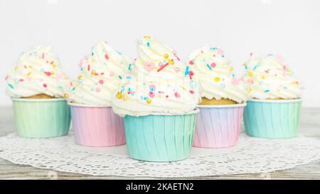 Les petits gâteaux à la vanille dans des gobelets en papier dégradé se dressent sur une serviette en dentelle en gros plan. Un plaisir magnifique pour les fêtes et les célébrations. Muffins à la crème au beurre d Banque D'Images