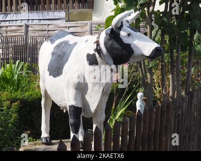 Une vache décorative grandeur nature avec cloche, donnant sur une clôture de jardin en bois Banque D'Images