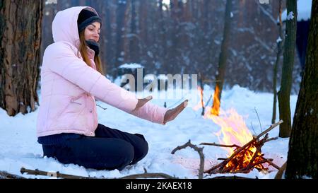 Jeune femme sur un pique-nique d'hiver dans la forêt se réchauffant près du feu. Banque D'Images